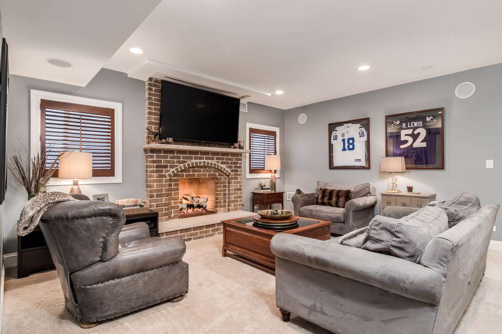 man cave living room with television mounted above a lit fireplace